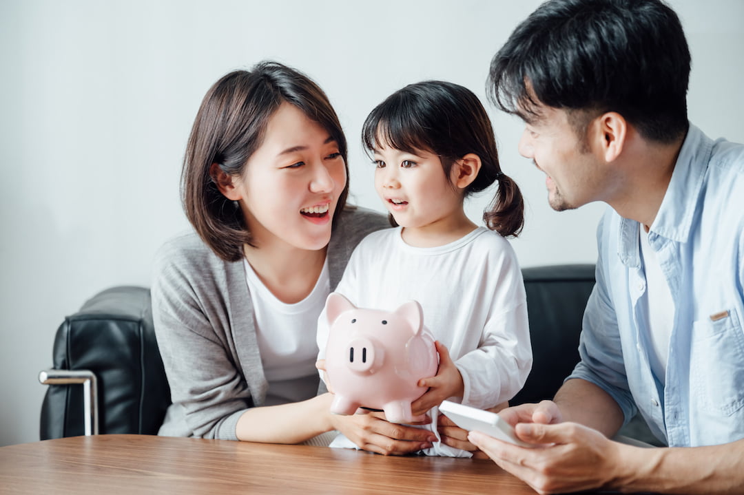family and daughter smiling at piggy bank | Featured Image For Saving as Much as Possible to Make a Deposit on a Home blog