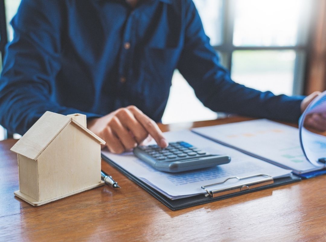 Mortgage broker using a calculator and contract | Featured image Real Estate as Part of Retirement Portfolio blog.