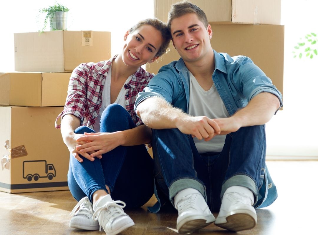 Couple smiling with boxes in the background | Featured image First Home Buyer FAQ blog.