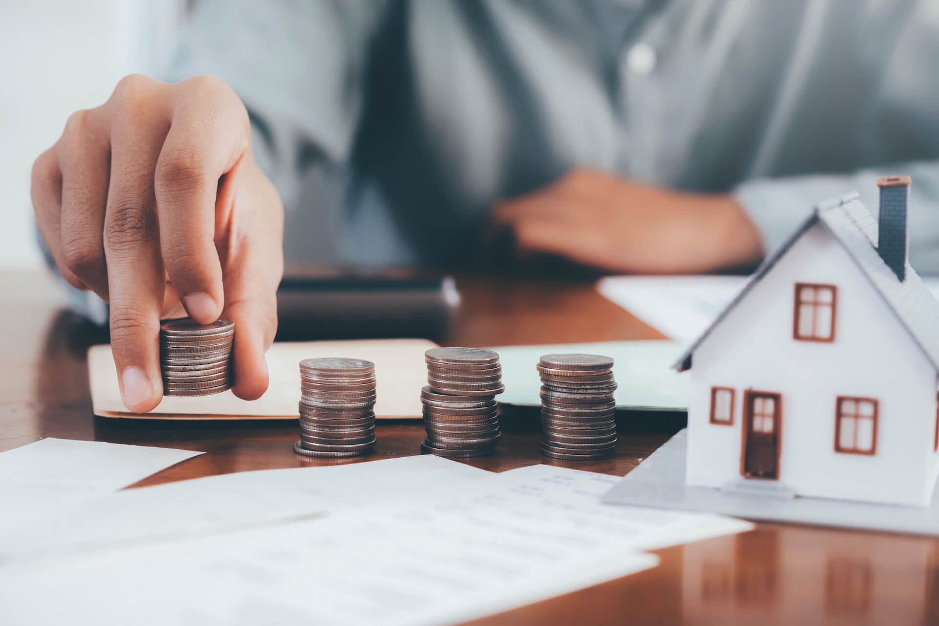 Photo of four columns of coins to the left of a small model house | Featured image for What is Negative Gearing - Understanding Negative Gearing Blog.